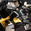 A Stena Recycling expert wearing protective gloves sorts a container of used mobile phones